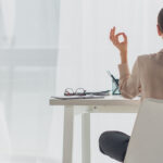 panoramic shot of businesswoman meditating in lotus pose with gyan mudra at workplace with incense stick